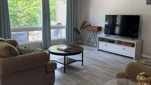 A living room with a sofa, coffee table, TV, and a balcony with curtains. - Relax with Nature (Coldwater)