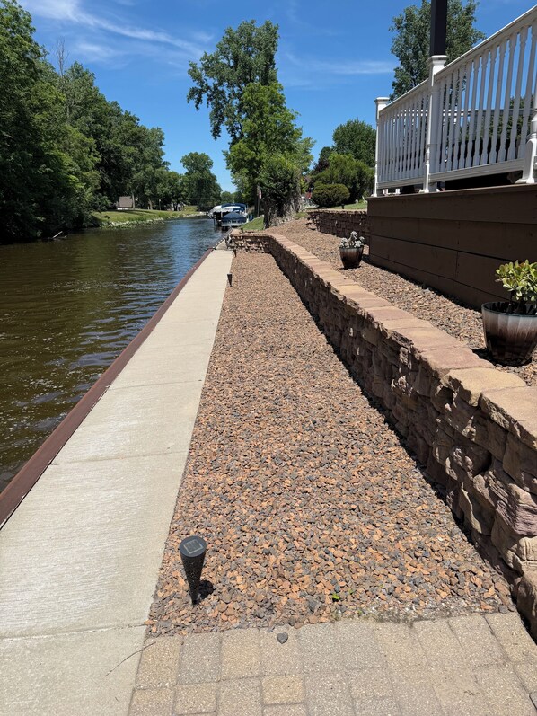 A riverside walkway with a stone wall, a concrete path, and a white fence.