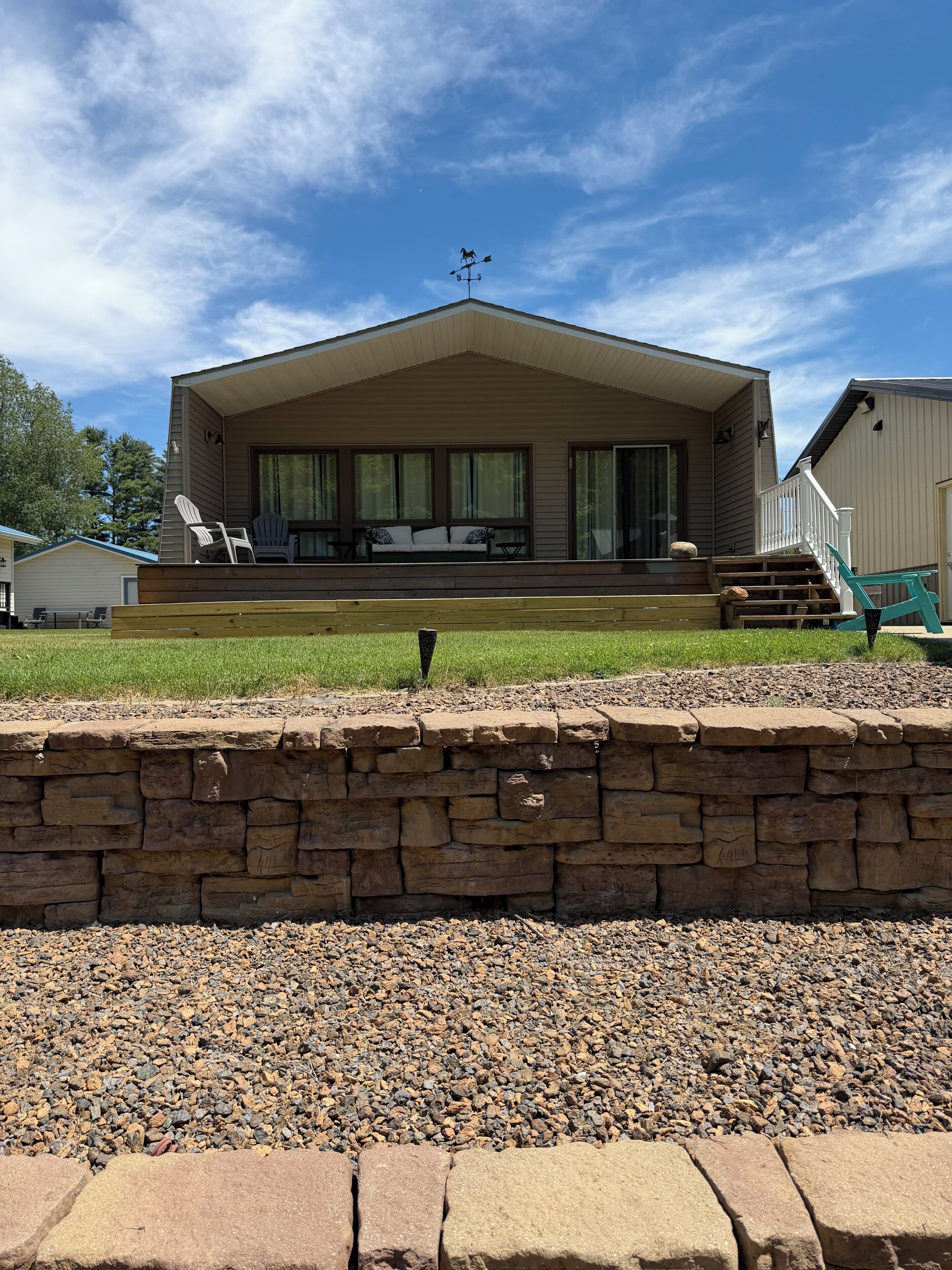 A single-story house with a porch, a stone wall in the foreground, and a clear sky.