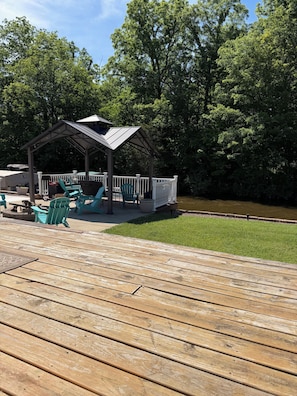 A wooden deck with a covered seating area, a small fire pit, and a pond.