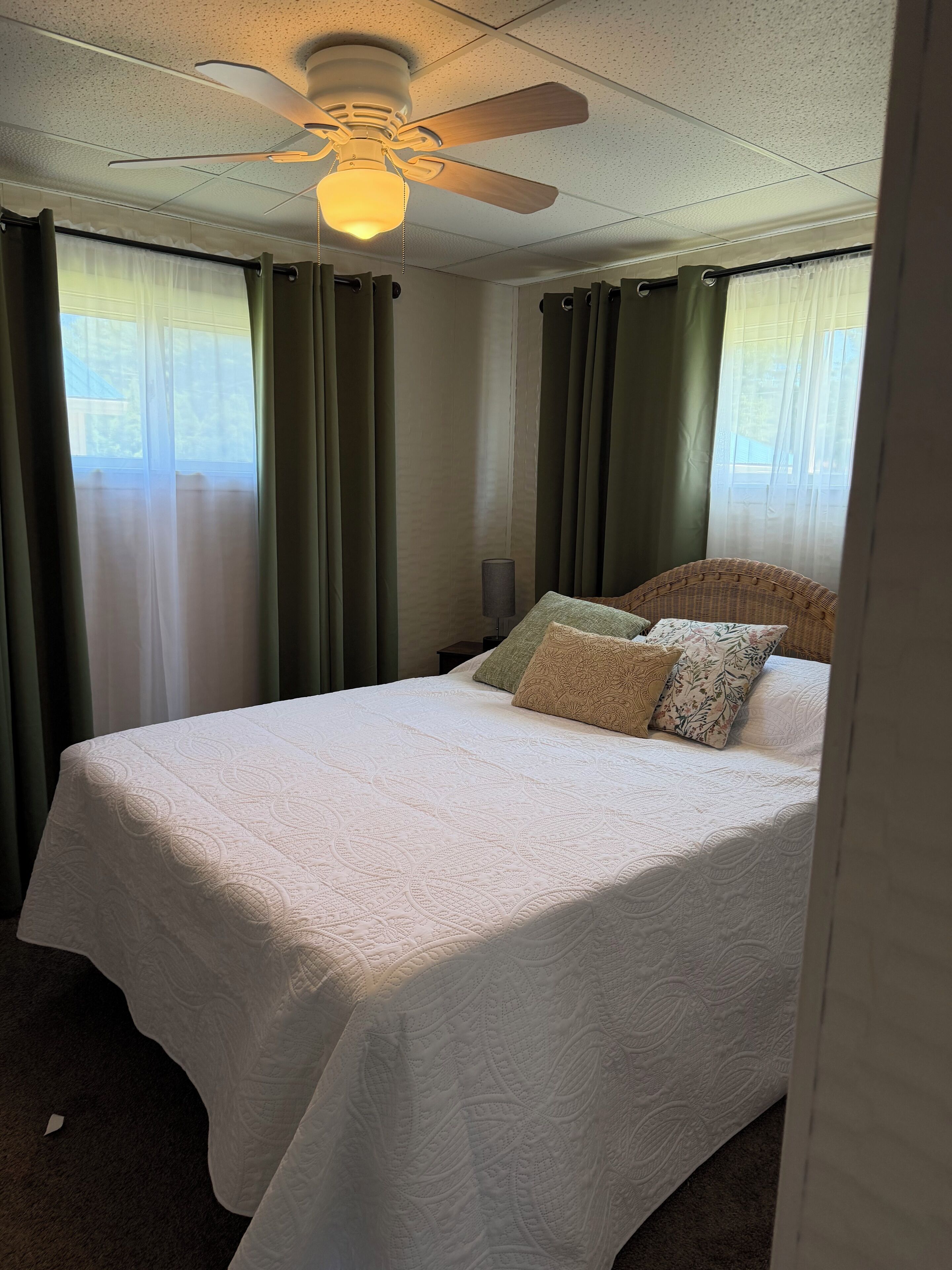 A hotel room with a bed, a ceiling fan, and sheer curtains.