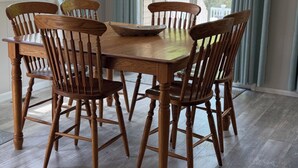 A dining area with a wooden table and chairs, large windows with curtains, and a view of greenery outside. - Relax with Nature (Coldwater)
