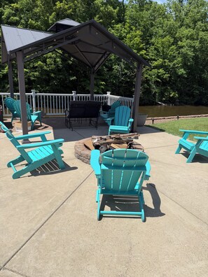 A covered outdoor seating area with Adirondack chairs, a grill, and a view of a river. - Relax with Nature (Coldwater)