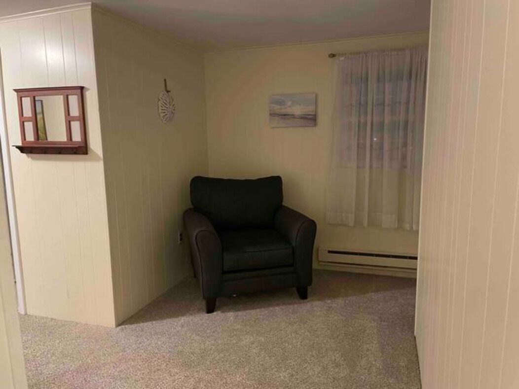 Een kamer met een donkerbruine leren fauteuil, een klein fotolijstje aan de muur, en een raam met dunne gordijnen.