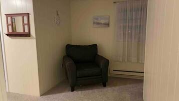 Een kamer met een donkerbruine leren fauteuil, een klein fotolijstje aan de muur, en een raam met dunne gordijnen.