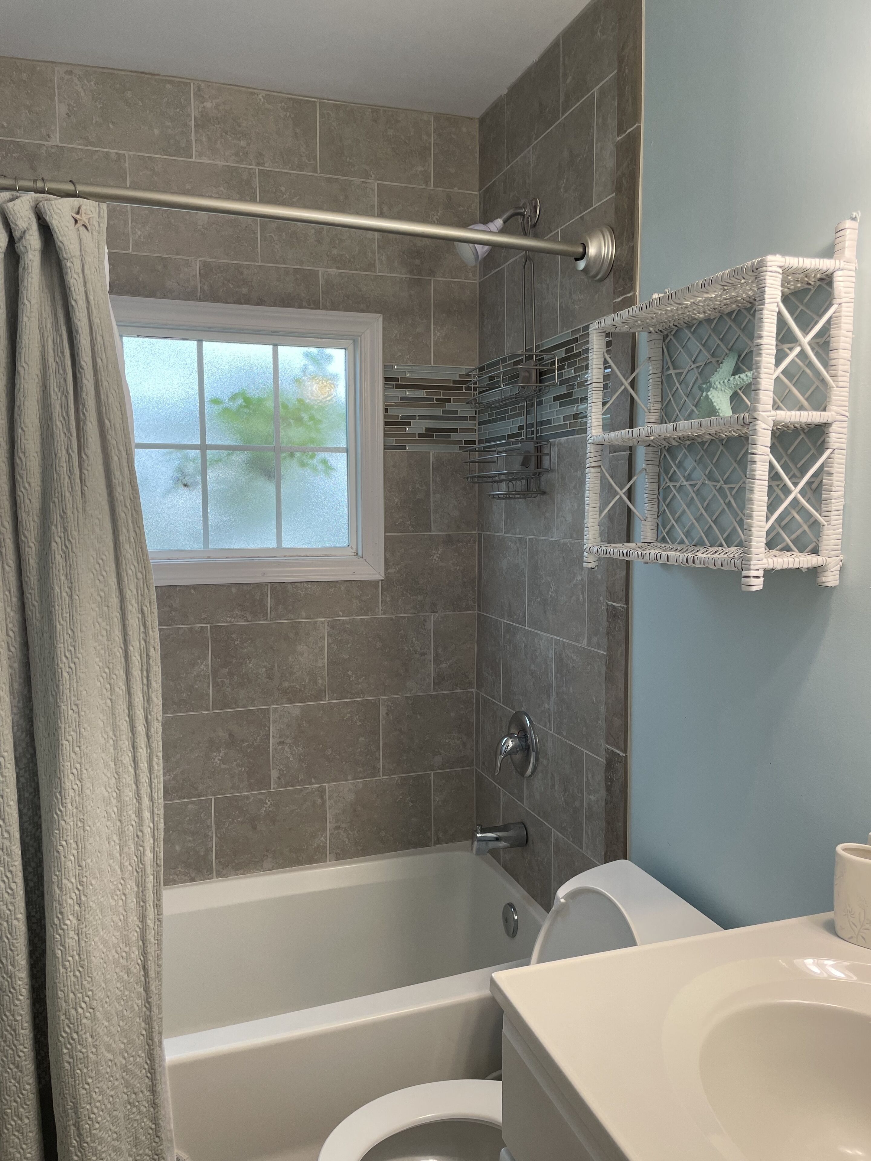 Un baño con bañera, inodoro y ventana con vidrio esmerilado.