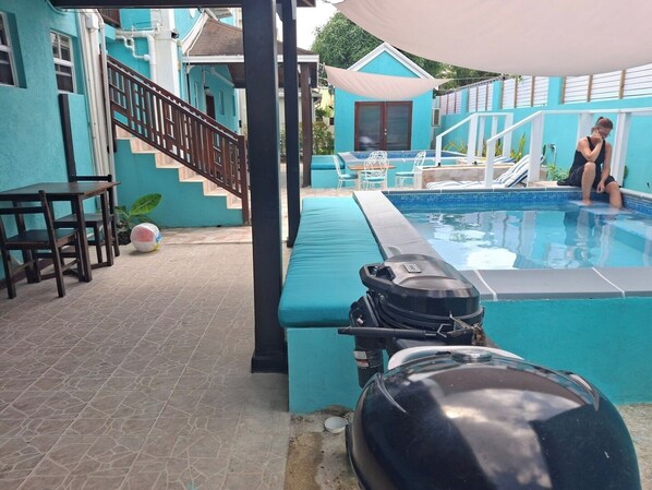 Zona de piscina con un área de estar techada, una escalera y una parrilla para barbacoa.
