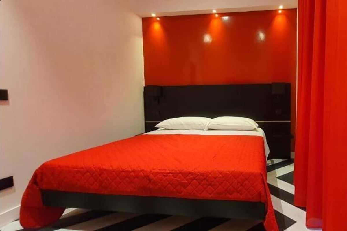 A bed with a red bedspread, a black headboard, and a white pillow.