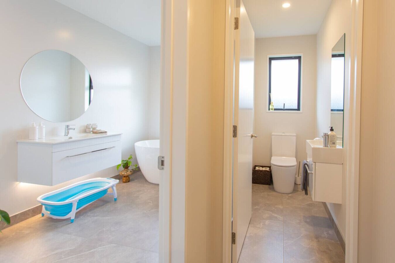 Une salle de bain moderne avec un meuble-lavabo blanc, un grand miroir, une baignoire et une petite baignoire bleue pour enfants.