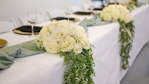 Une table dressée avec des nappes blanches, des roses blanches et des éléments de verdure.