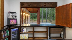 Un espace bar avec vue sur la forêt, un appareil à smoothies de la marque Royal Ice et un réfrigérateur à bière Franzia.