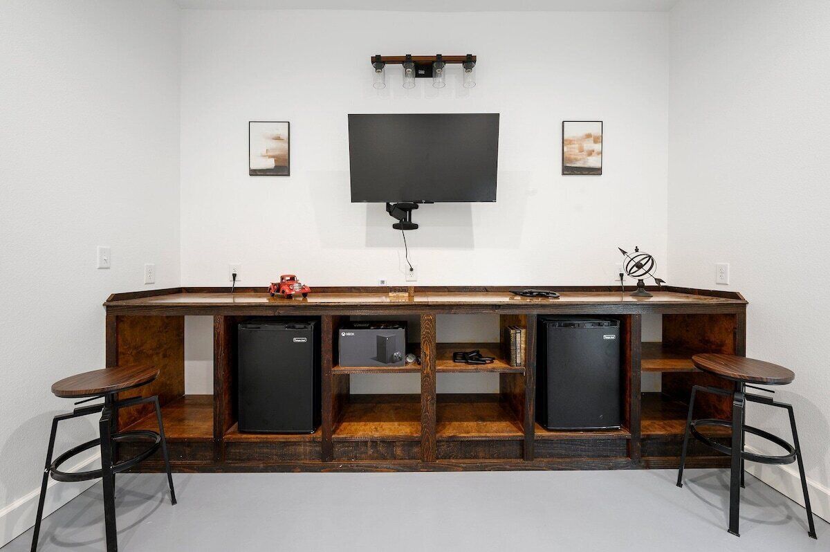 A bar area with a flat-screen TV, wooden bar counter, and two stools.