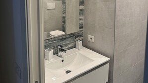 Une salle de bain moderne avec un lavabo blanc, un miroir et des murs recouverts de carreaux gris.