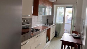 Une cuisine compacte équipée d’un réfrigérateur, d’un four et d’un évier. On y trouve une table à manger avec des chaises et une fenêtre avec des rideaux.