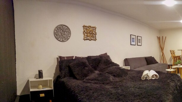 Ein Schlafzimmer mit Bett, Nachttischen, Schreibtisch und Stuhl. An den Wänden befinden sich Dekorationen und eine Tür zu einem weiteren Raum.