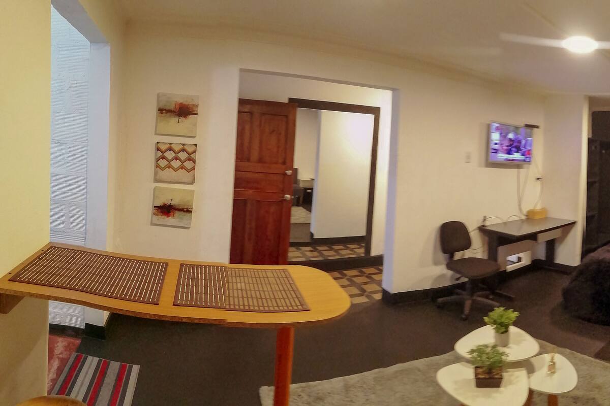 A living room with a wooden table, a sofa, a TV, and a desk.