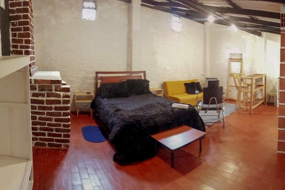 A room with a bed, a yellow chair, a desk, and a brick wall.