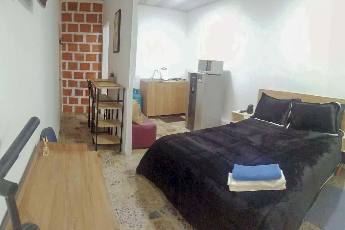 A hotel room with a bed, a desk, a chair, a wardrobe, a small table, and a radiator.