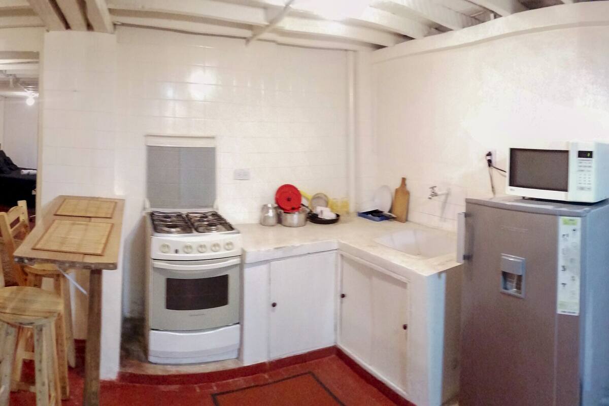 A compact kitchen with a stove, microwave, and cabinets. There is a yellow sofa and a small dining table with chairs.