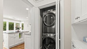 A laundry room with two stacked front-loading washers and dryers, white cabinetry, and a window with a view of greenery. - Charming Historic Marietta Home! (Marietta)
