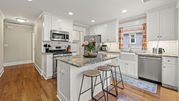 A modern kitchen with white cabinets, granite countertops, stainless steel appliances, and a central island with bar stools. - Charming Historic Marietta Home! (Marietta)