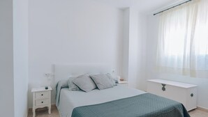 Un dormitorio minimalista con cama, mesitas de noche y una ventana con cortinas.