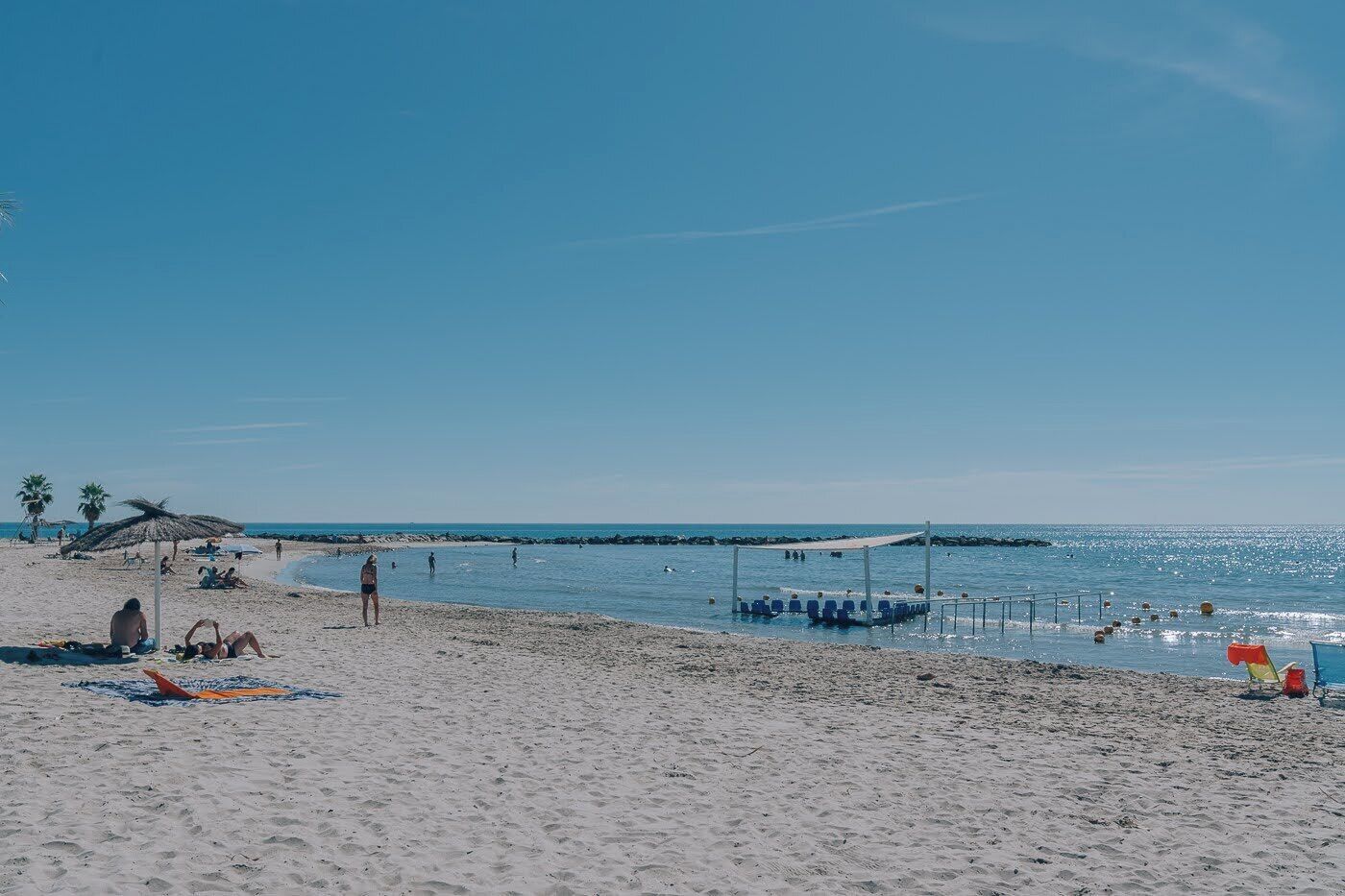 Una playa con gente tomando el sol, una red de voleibol y palmeras.