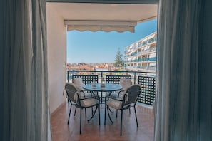 Un balcon avec une table et des chaises, une vue sur les immeubles et un ciel dégagé.