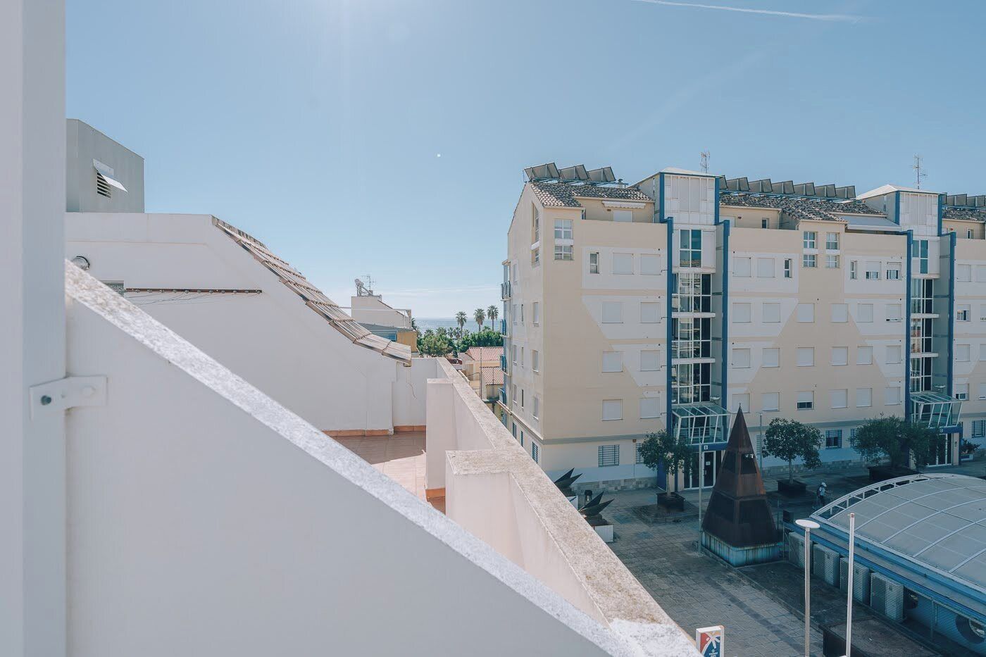 A multi-story residential building with balconies, a covered outdoor area, and a clear sky.