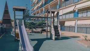 Un parque infantil con toboganes y escaleras, rodeado de edificios de varios pisos con balcones.