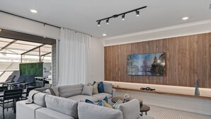 A modern living room with a sectional sofa, a dining area with chairs, a green wall, and a wooden panel wall with a painting.
