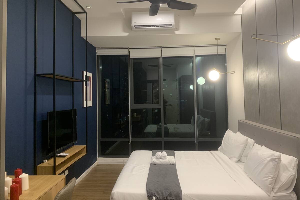 Een moderne hotelkamer met een groot bed, een plafondventilator, een airconditioningapparaat, een televisie op een standaard en uitzicht door een glazen deur.