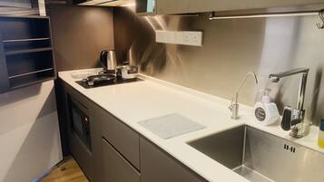 A modern kitchen with a stainless steel sink, a kettle, and a hand soap dispenser.
