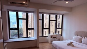 A modern hotel room with a large bed, a desk, and two windows offering city views. - Ceylonz Suites by Roomy (Kuala Lumpur)