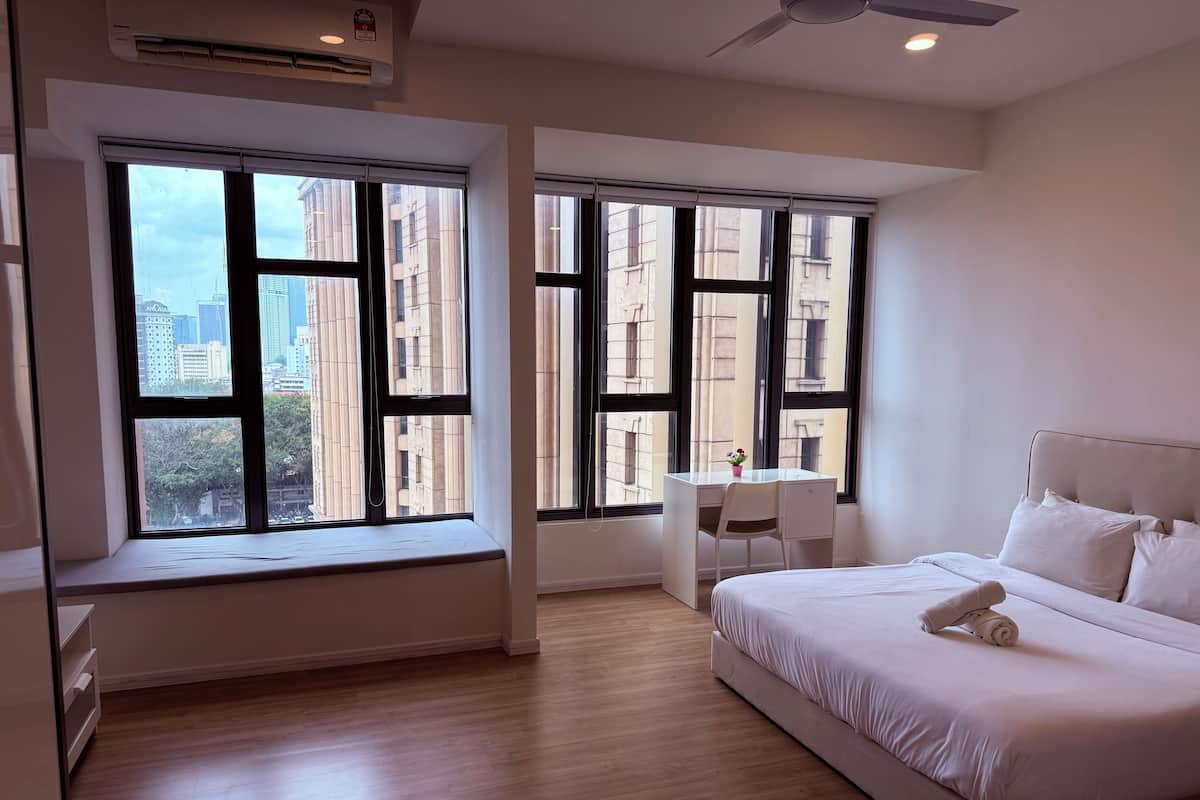 Een moderne hotelkamer met een groot bed, een bureau en twee ramen met uitzicht op de stad.