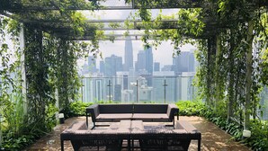 A wooden deck with a bench and a view of a city skyline through a green trellis structure. - Ceylonz Suites by Roomy (Kuala Lumpur)