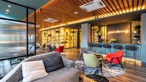 A modern lounge area with a sofa, chairs, a bar, and a bookshelf. - Ceylonz Suites by Roomy (Kuala Lumpur)