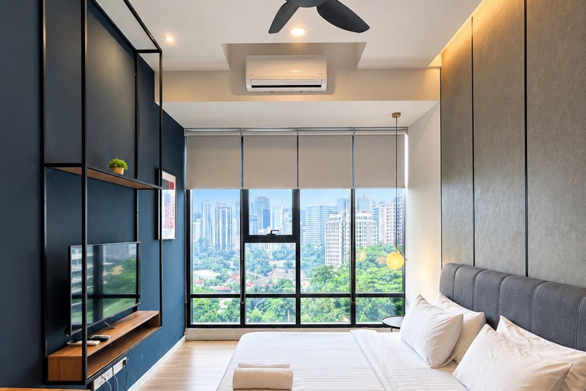 A modern bedroom with a large bed, a desk, and a view of a cityscape.