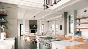 A modern kitchen with white cabinetry, a large island, and a dining area with wicker chairs. - Stunning Marsh View Pool Retreat on St. Simons Island (St. Simons Island)