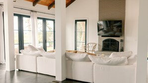 A modern living room with a white sofa set, a fireplace, and a large TV mounted on the wall. - Stunning Marsh View Pool Retreat on St. Simons Island (St. Simons Island)