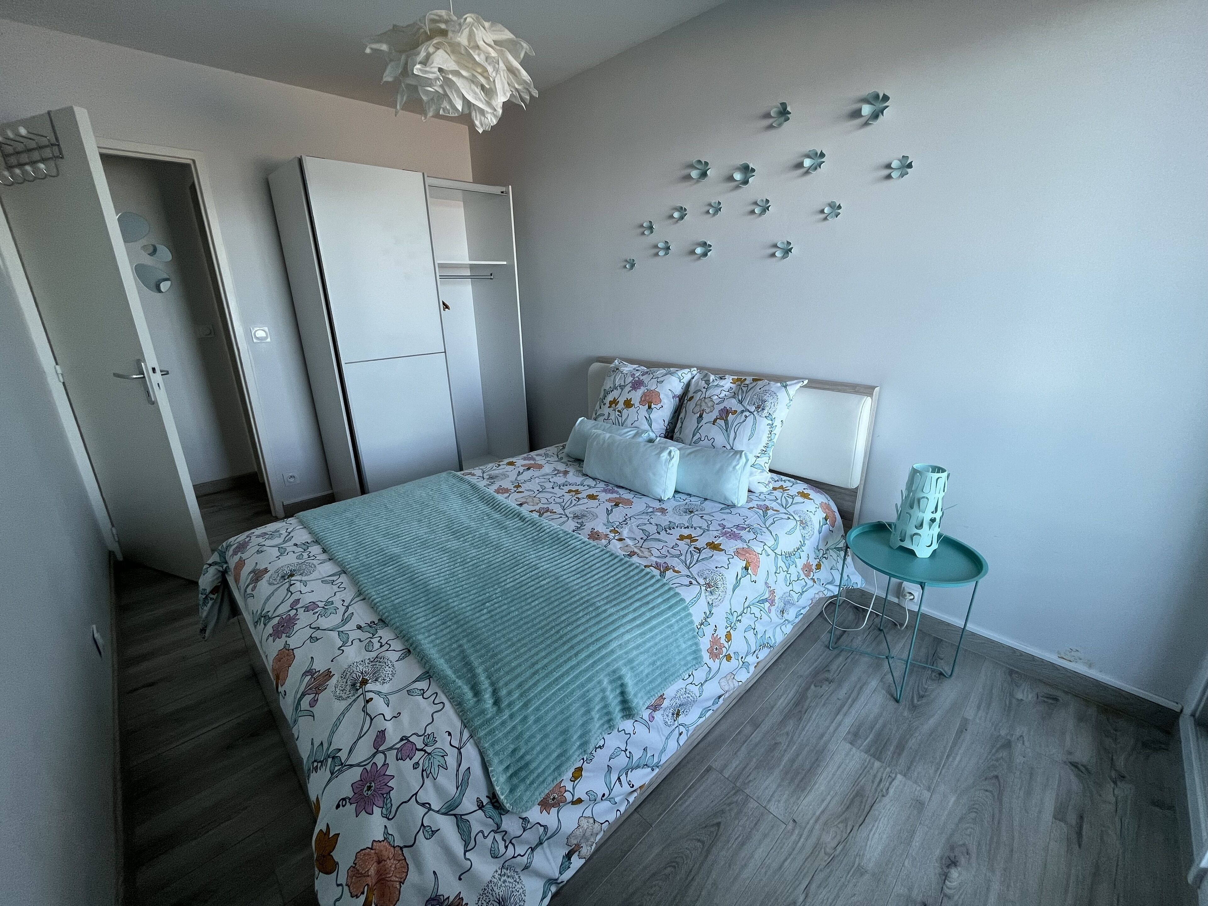 A bedroom with a bed, a wardrobe, a bedside table, and a wall-mounted light fixture.