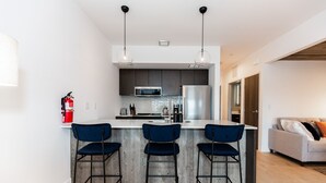 A modern kitchen with a central island, bar stools, and a microwave. - Style Points Shelter: Downtown (Bozeman)
