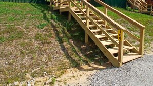 Une série d’escaliers en bois mène à des cabanes en rondins, entourées de clôtures vertes.