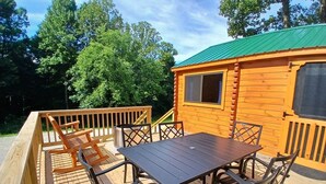 Une terrasse en bois avec une table et des chaises, une poubelle en métal et un chalet doté d’un toit végétalisé.