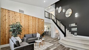 A modern living room with a grey sofa, a coffee table, and a wooden accent wall. - Private Oasis On 2 Acres w/ Indoor Pool & Theater! (Eagle)