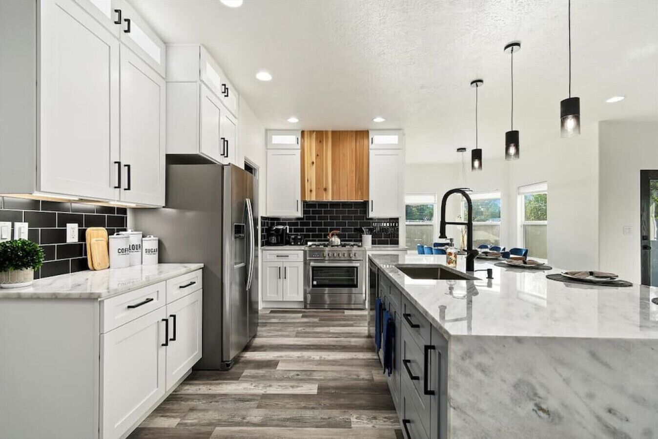 Una cocina moderna con armarios blancos, un refrigerador de acero inoxidable, techo de madera y una isla grande con pileta.