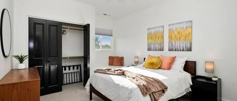 A bedroom with a bed, bedside tables, a ceiling fan, and artwork on the wall.