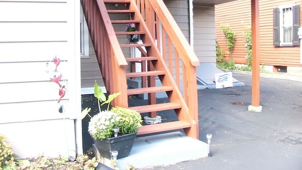 Eine Holztreppe führt zu einer überdachten Veranda, am Fuß befindet sich ein Blumentopf.