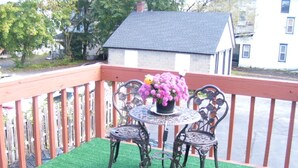 Eine Terrasse mit Kunstgrastrittichkeit, zwei Metallstühlen und einem Tisch mit einem Blumentopf.