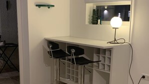 Ett litet pentry med en vit bänkskiva, två svarta barstolar, en spegel och en väggmonterad lampa.